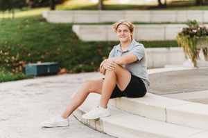 Person sitting on concrete steps wearing athletic wear and white sneakers in an outdoor setting.