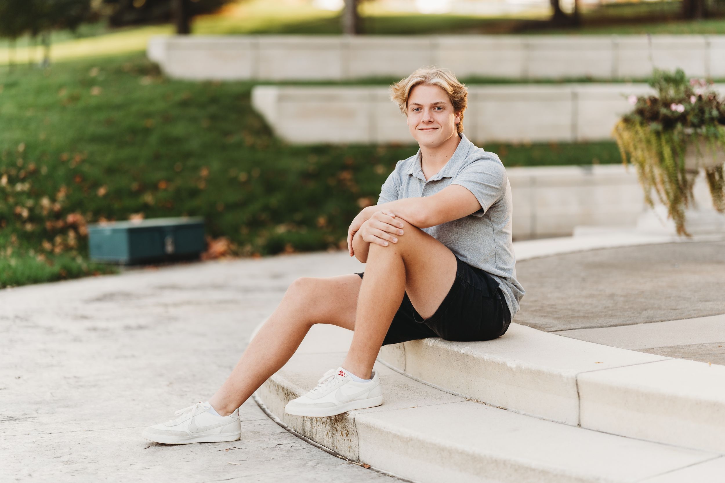 Person sitting on concrete steps wearing athletic wear and white sneakers in an outdoor setting.
