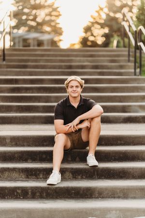 Person in black athletic wear sits casually on concrete steps during golden hour sunset.