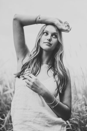 Black and white portrait of a person with long blonde hair posing outdoors in a light colored top with delicate jewelry.