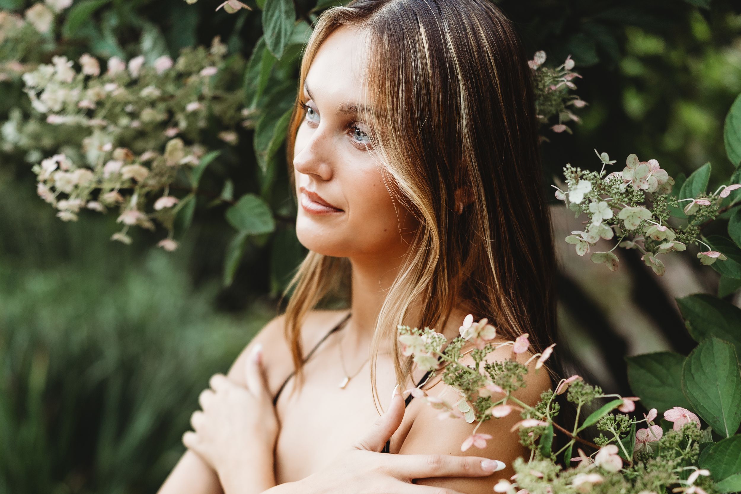 Woman in white dress poses among blooming dogwood flowers in a spring garden setting.