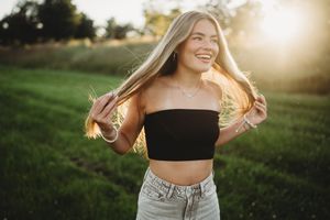 Woman in casual outfit dancing and twirling in a sunlit grassy field during golden hour.