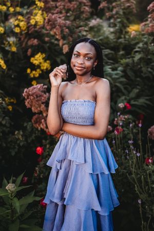 A light blue ruffled sundress is showcased in a garden setting with yellow and pink flowers in the background.