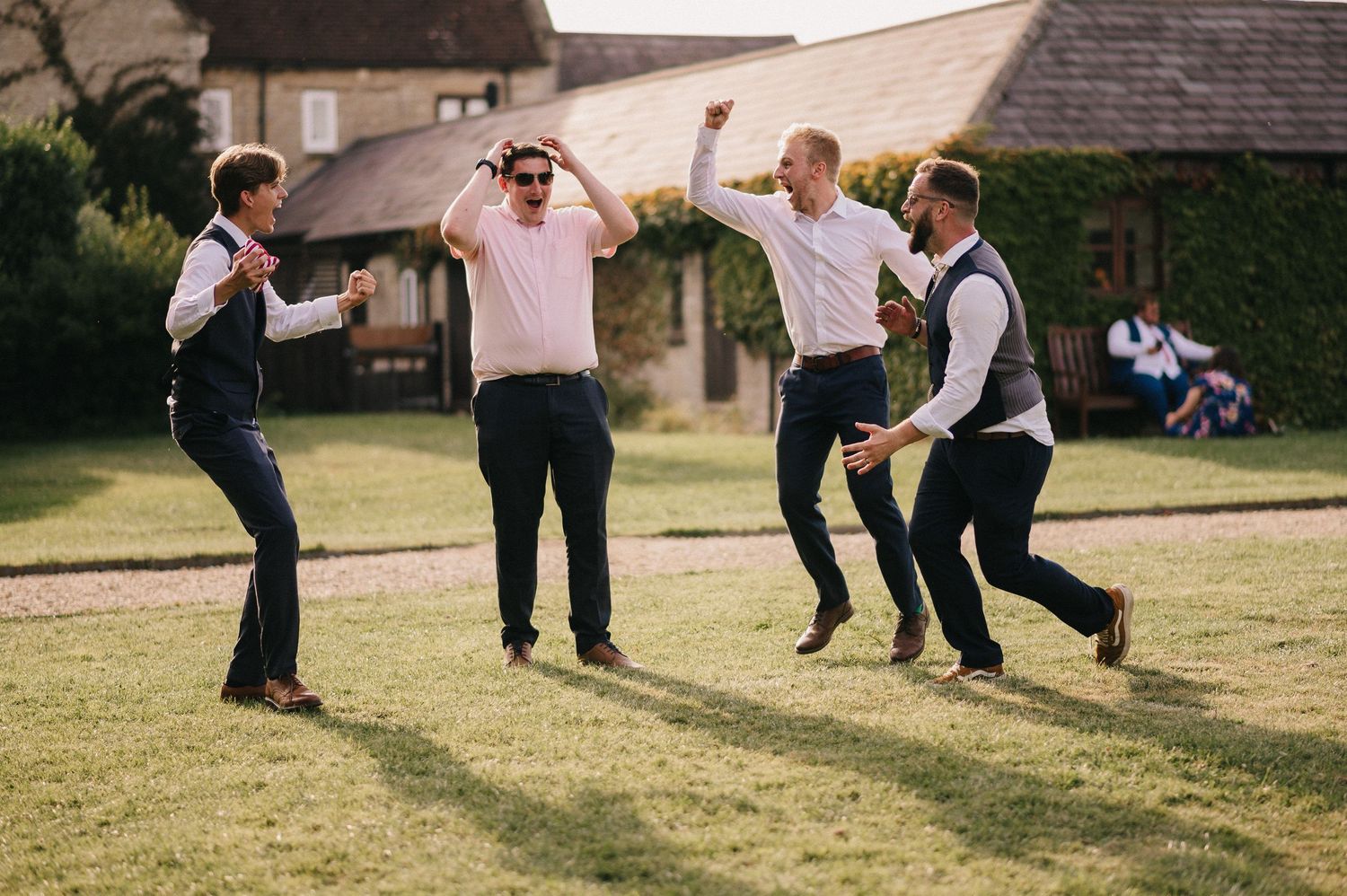 Four people joyfully jumping and dancing together on a grassy lawn during a sunny outdoor celebration.