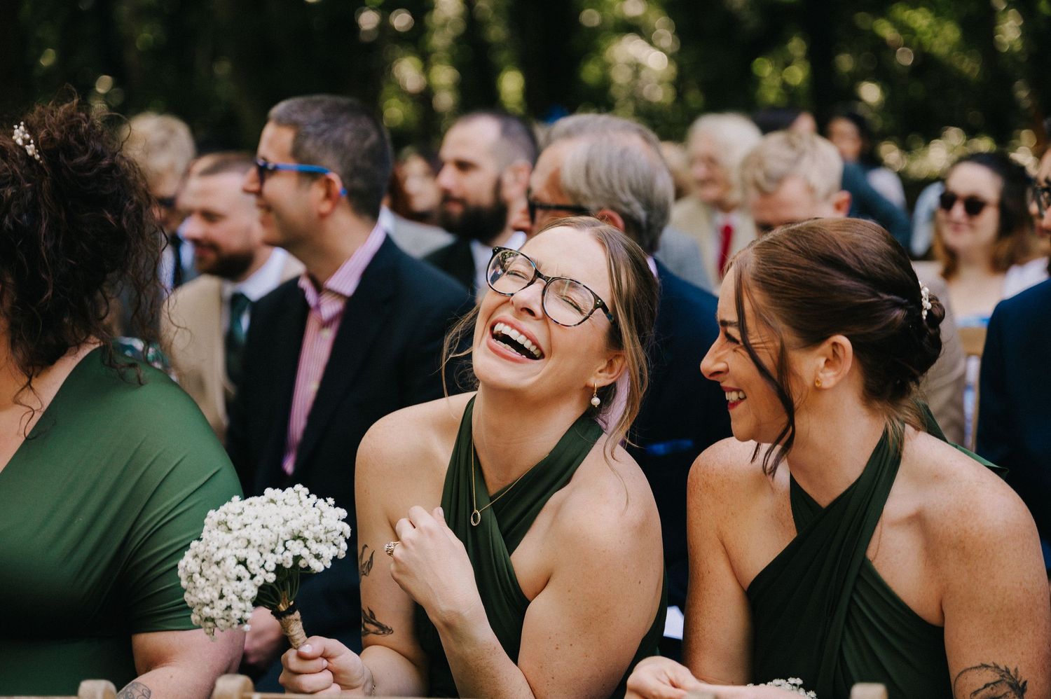Bridesmaids in dark green halter dresses share a joyful moment during an outdoor wedding celebration.