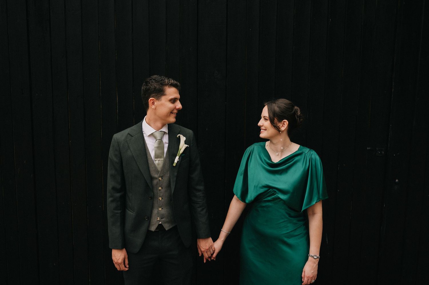 A couple in formal attire, with the woman wearing an emerald green dress and the man in a dark suit, share a candid moment.