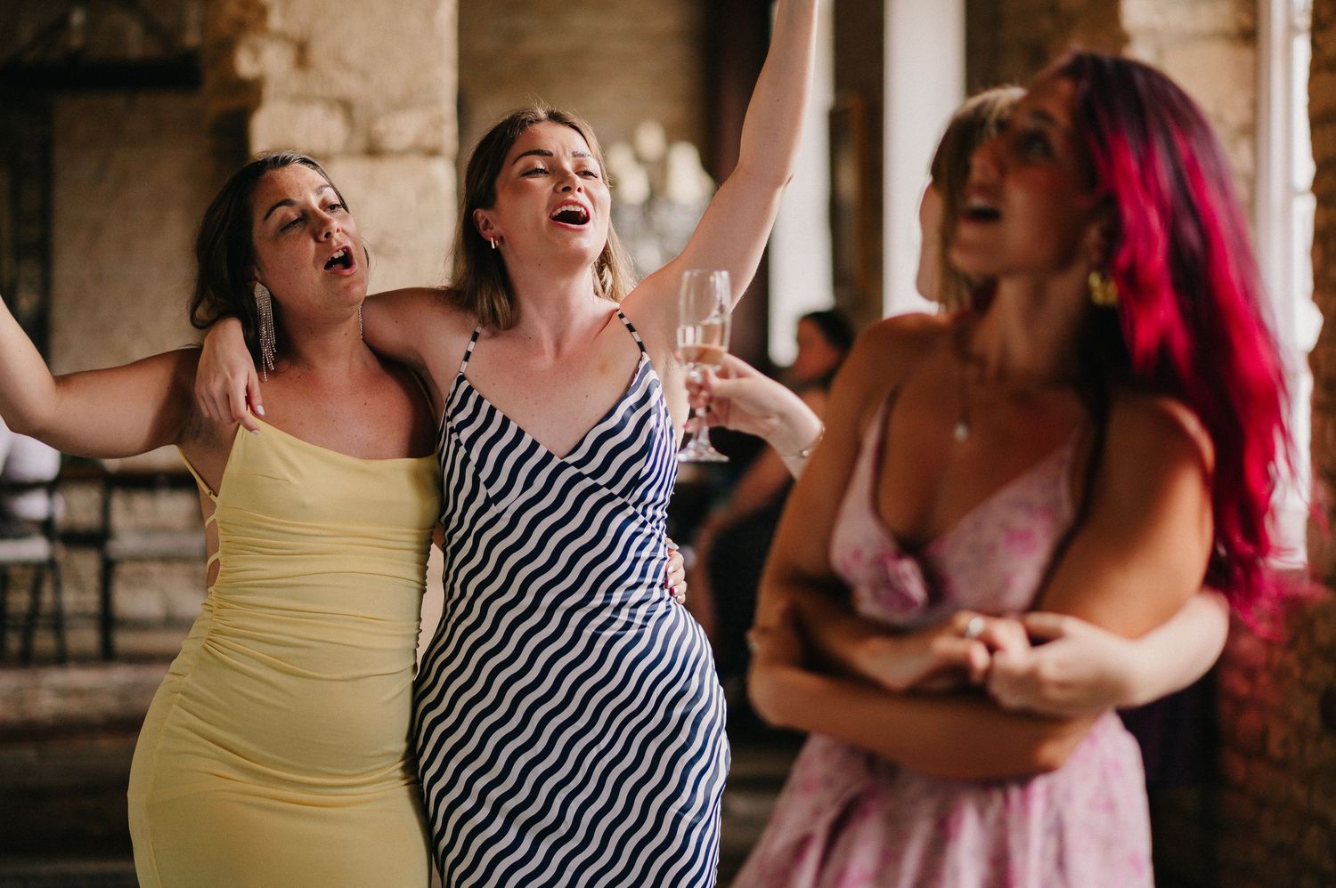 Group of friends laughing and enjoying a social gathering in an indoor setting with stone walls and warm lighting.