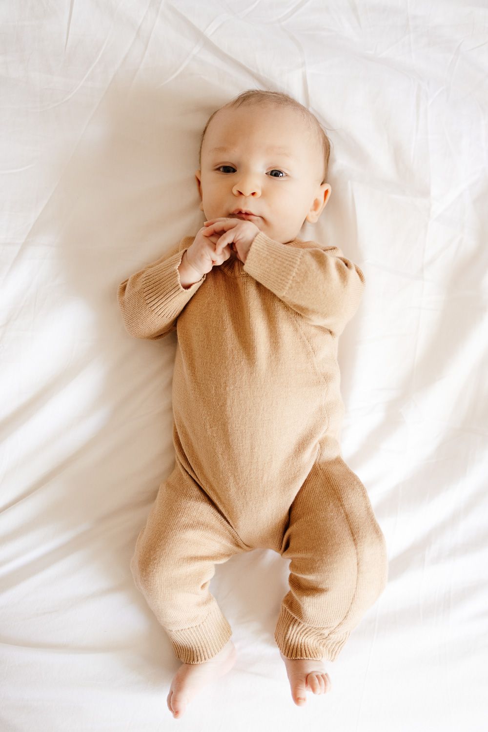 Baby lies on white bedding while looking into the camera