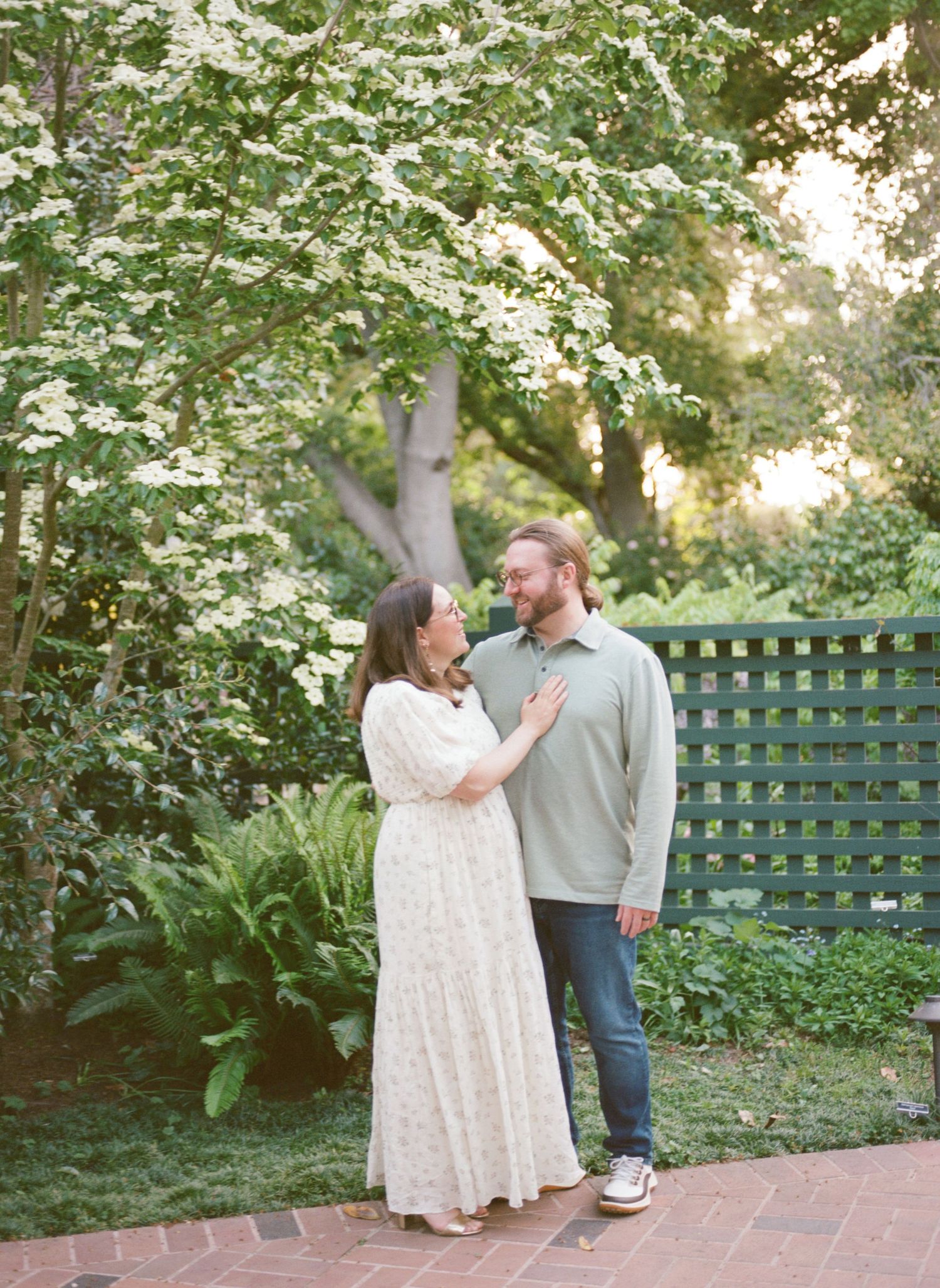 A couple shares playful moments in a garden setting while walking along a brick path at sunset.