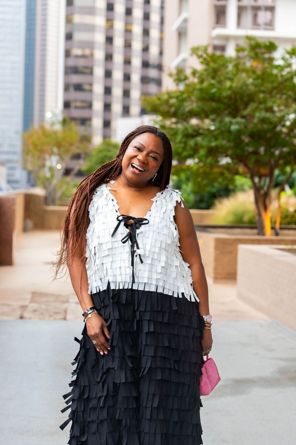 Person wearing a black and white fringe dress poses outdoors with city buildings in background.