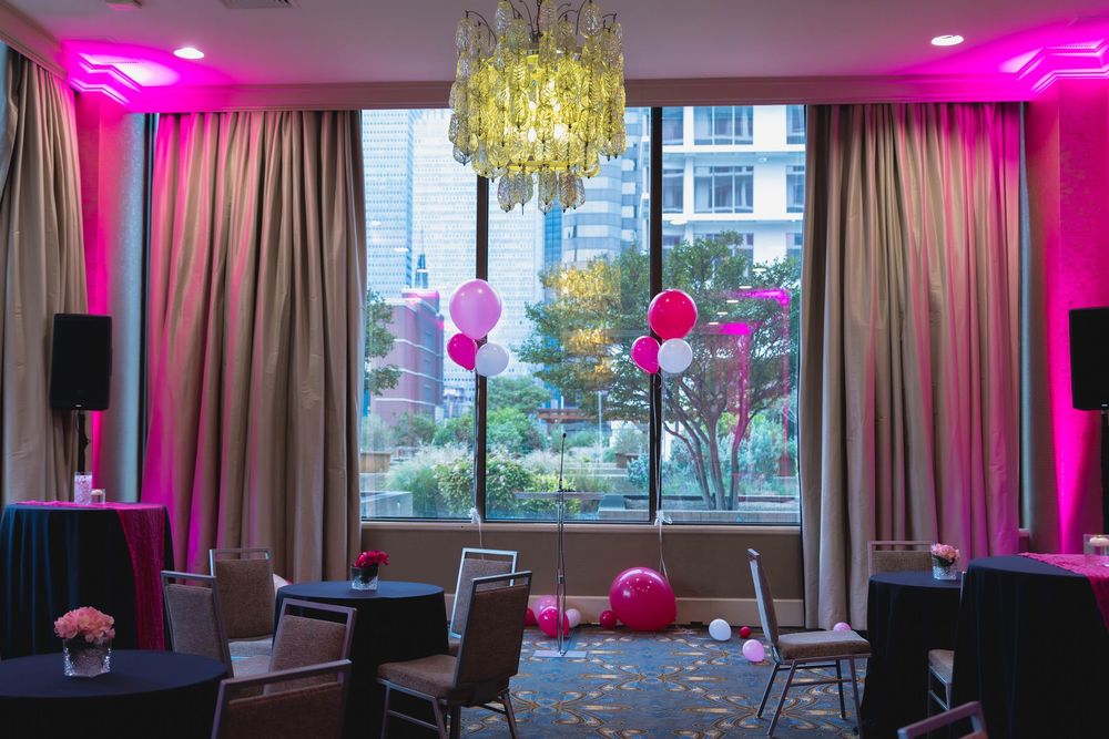 Modern event space with pink lighting, chandelier and window overlooking city.