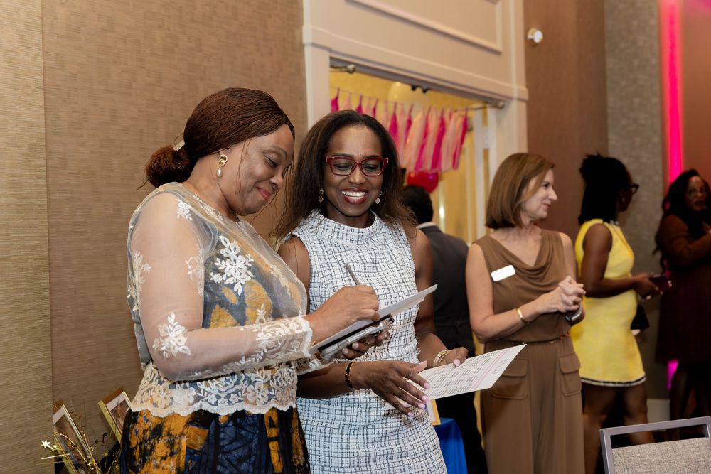 Event attendees reviewing materials together at an indoor celebration with pink accent lighting.