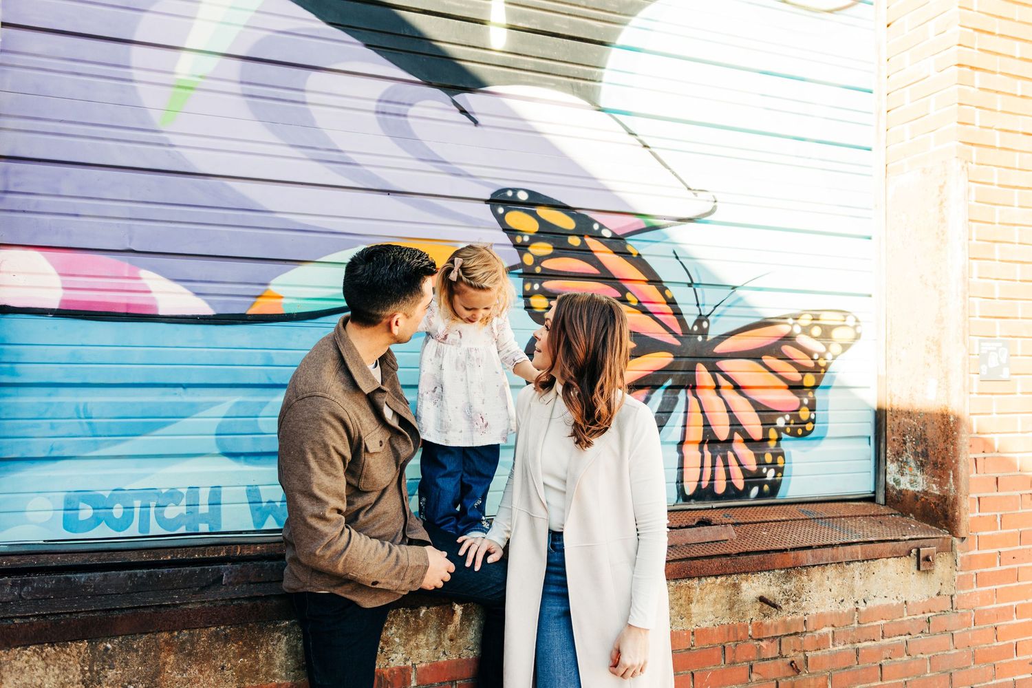 A family stands together against a colorful wall with butterfly street art mural in Camp North End.