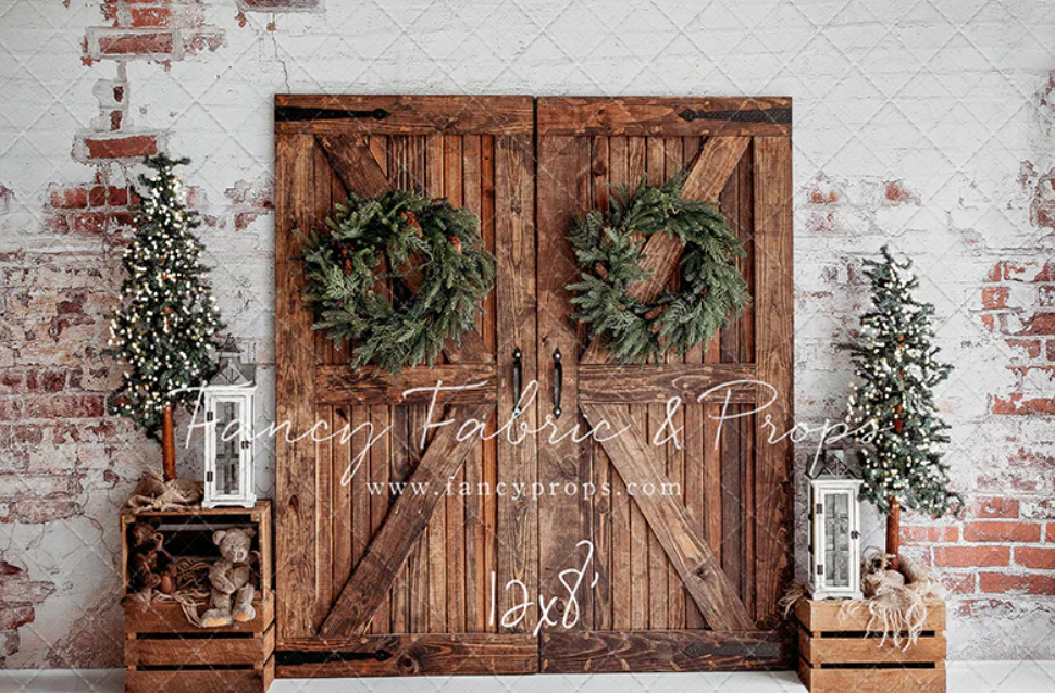 Rustic wooden barn doors with Christmas wreaths and garlands against a whitewashed brick wall create a festive backdrop.