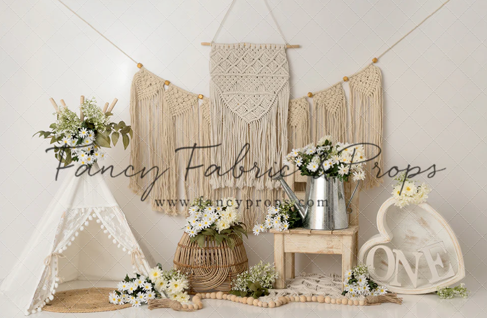 Boho-style photography setup with macrame wall hanging, floral arrangements, and vintage props against neutral backdrop.