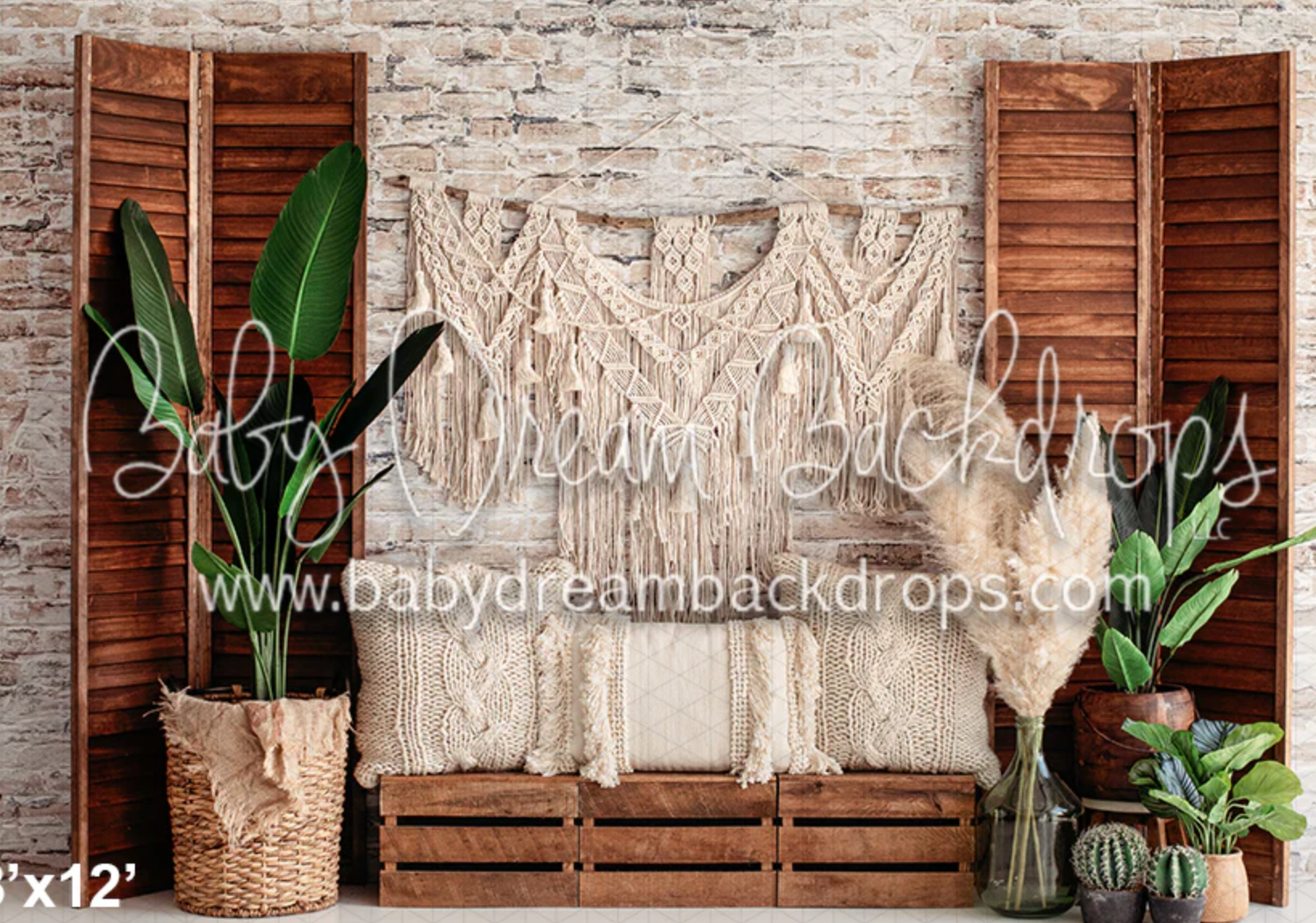 Boho-style photography backdrop with macrame wall hanging, wooden shutters, and potted tropical plants against brick wall.