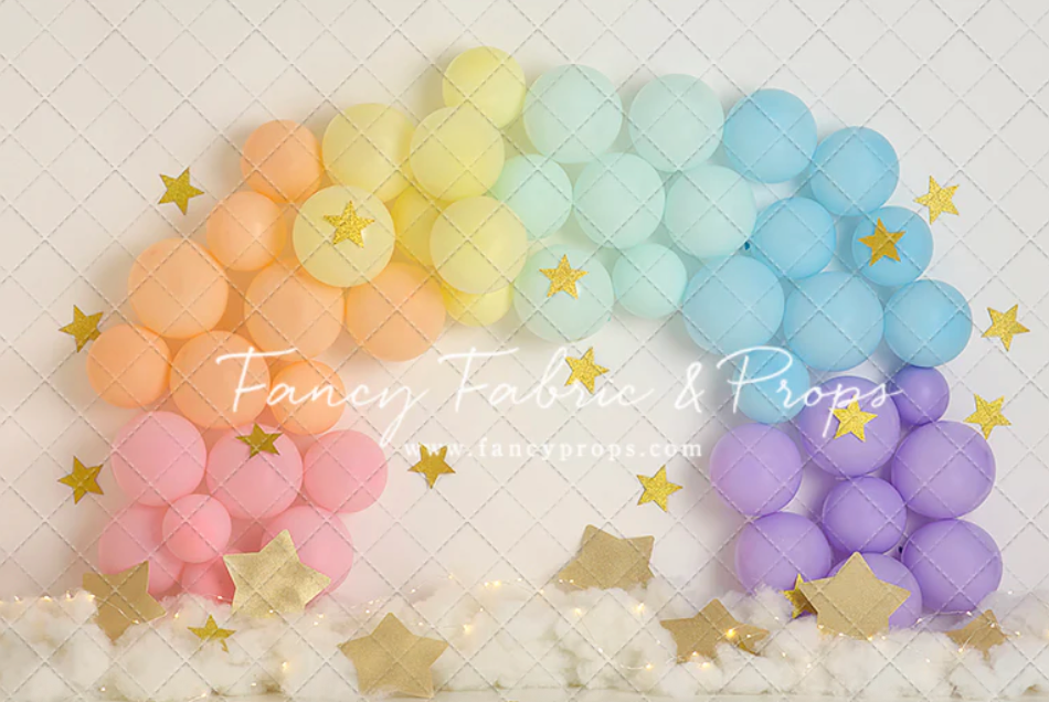 Pastel balloon arch with twinkling star decorations creates a dreamy rainbow effect against a light background.