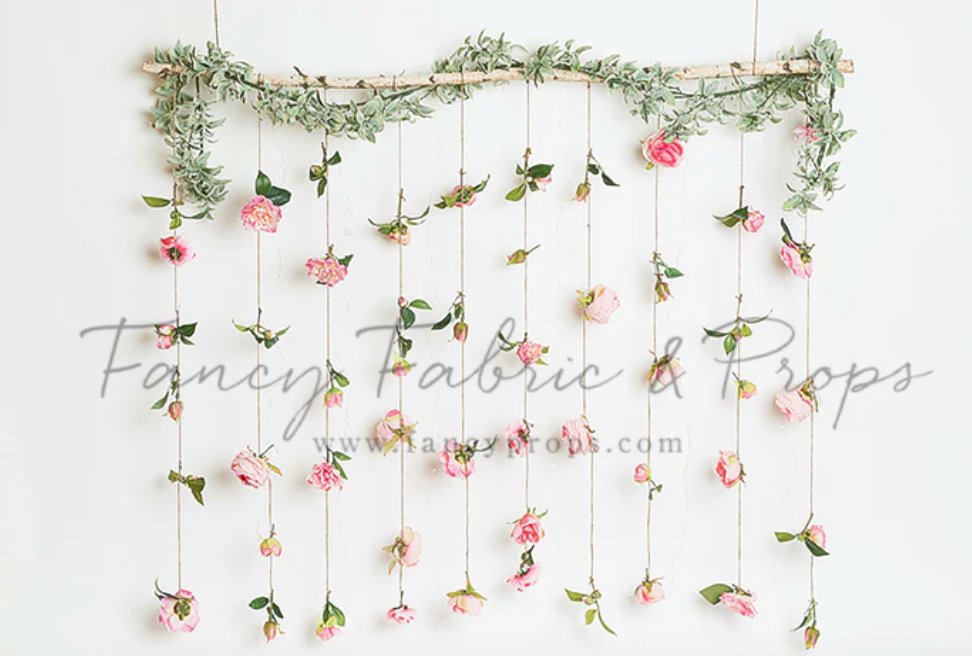 Pink roses and greenery hang from strings against a white background creating a delicate floral garland display.