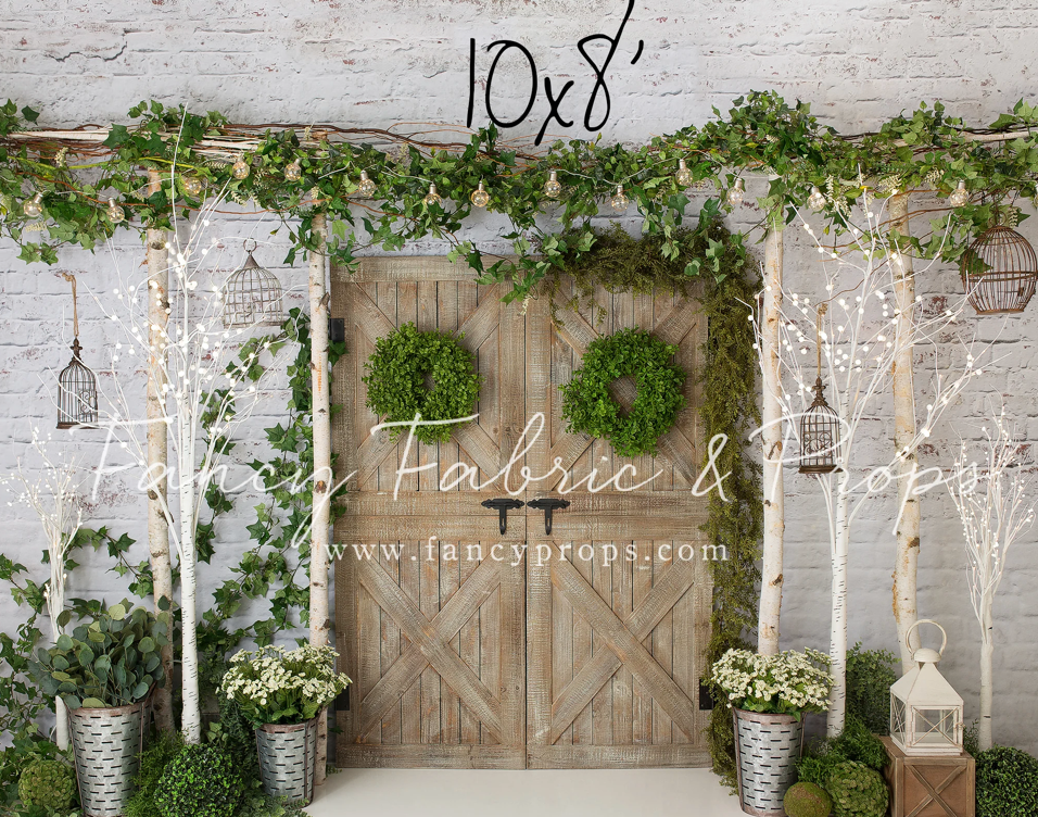A rustic wooden barn door backdrop adorned with white floral arrangements and greenery creates an elegant wedding setting.