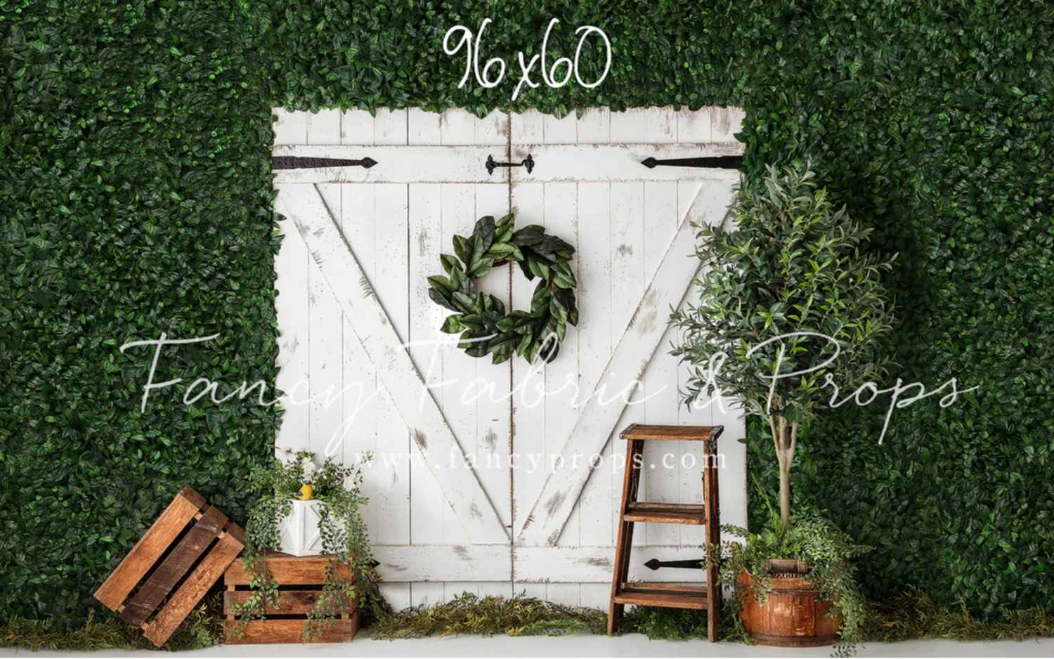 Rustic white barn door with wreath against green hedge backdrop, featuring wooden props and vintage decor elements.