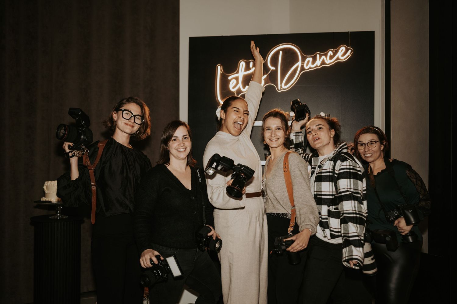 A group of people posing together at a dance event with a neon sign in the background.