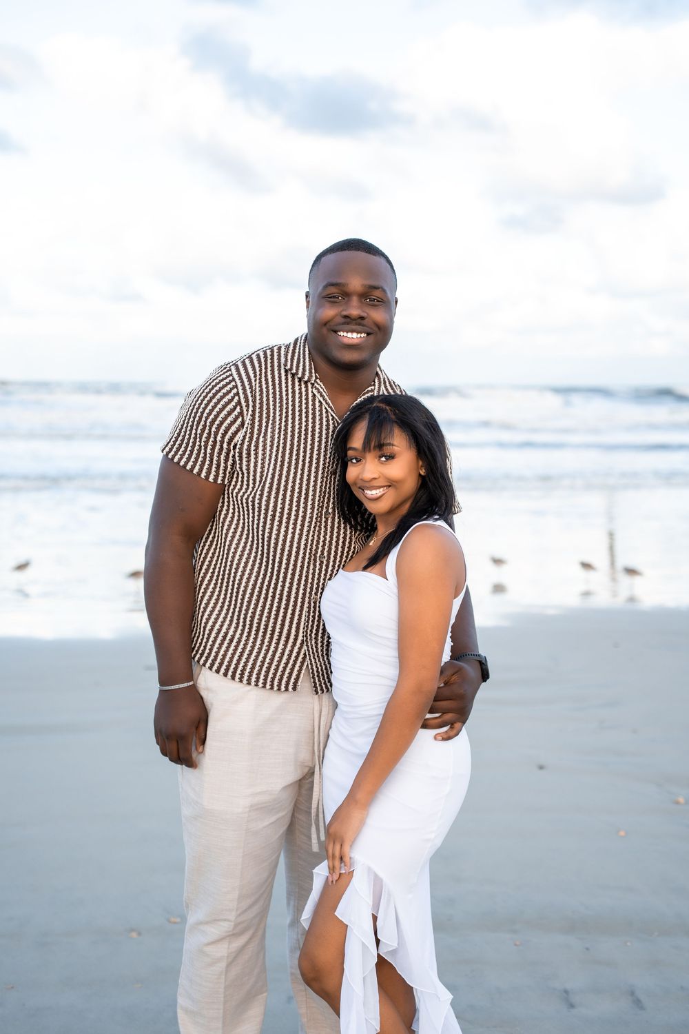A couple in coordinated outfits embraces and smiles while standing on a cloudy beach in Daytona Beach, Florida
