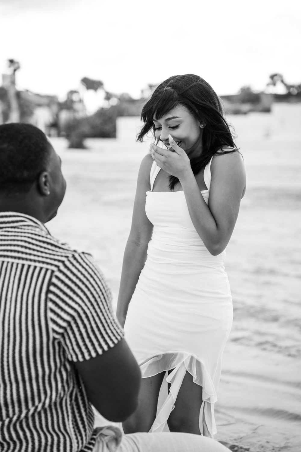 A black and white emotional moment of a beach proposal with the ocean and buildings in the background in Daytona Beach, Florida