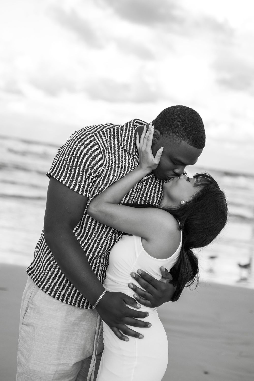 A romantic couple shares a tender moment in black and white photos at the beach wearing striped shirt and white dress in Daytona Beach, Fl
