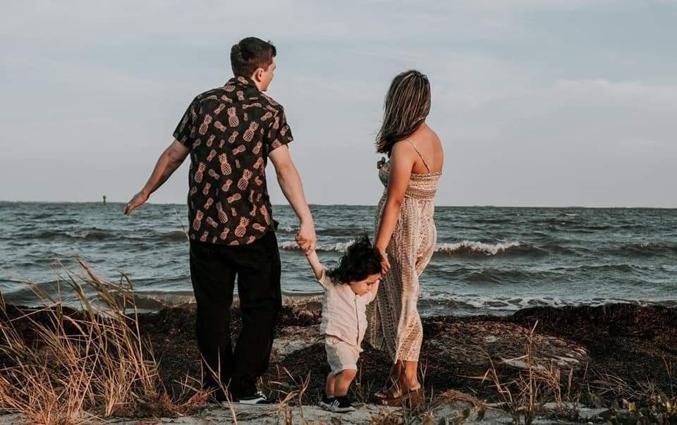 Family holding hands while standing on coastal rocks overlooking choppy ocean waves at sunset.