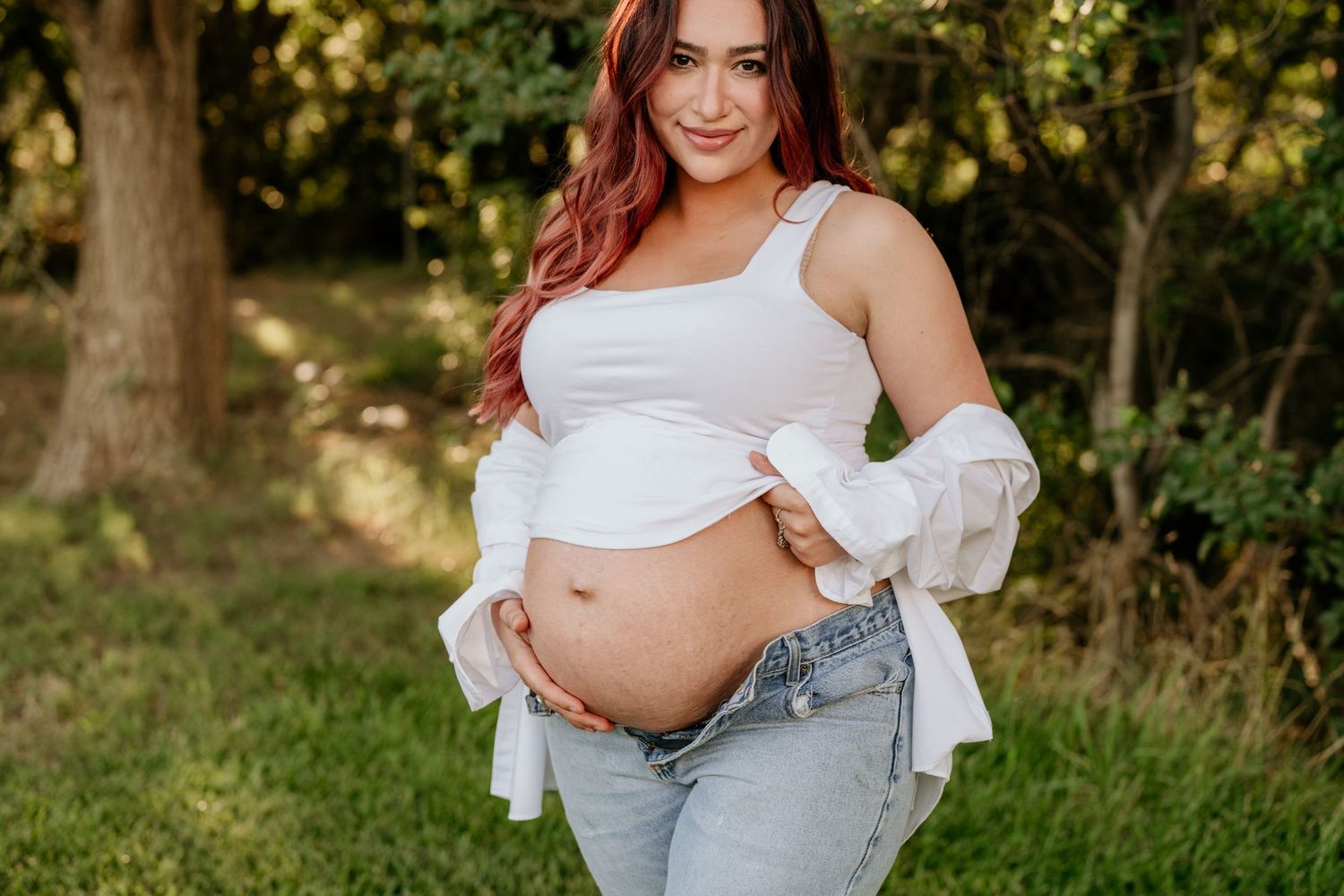 Maternity photo session outdoors with white crop top and denim in natural setting.