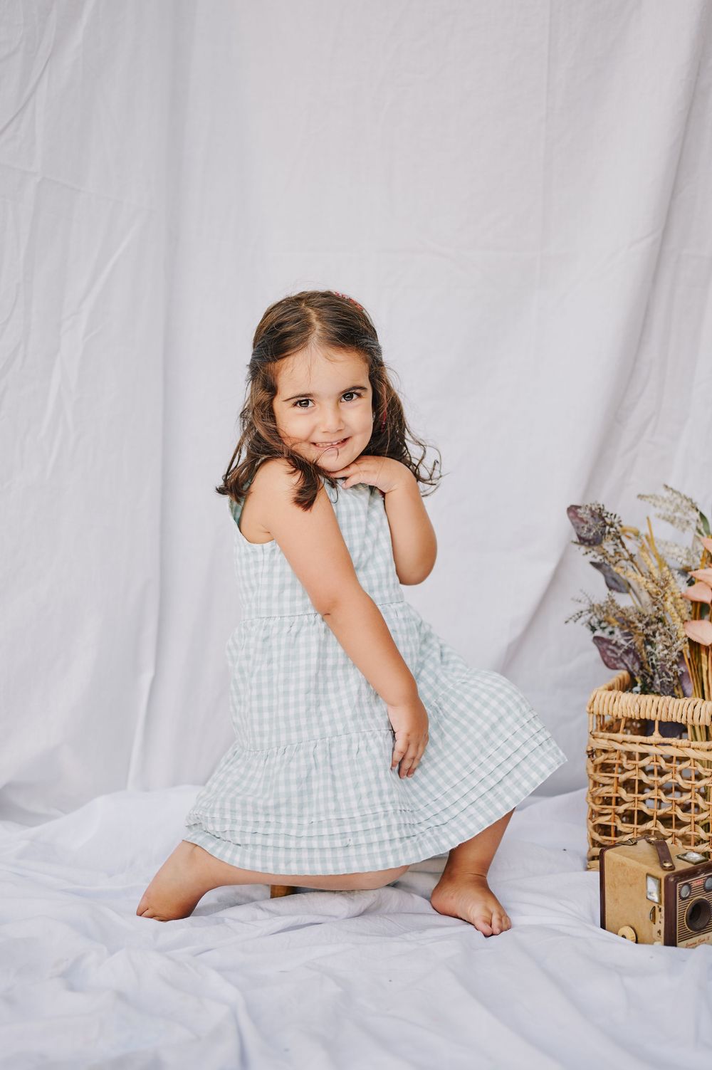 Smiling young girl twirling in sage green gingham dress barefoot indoors.