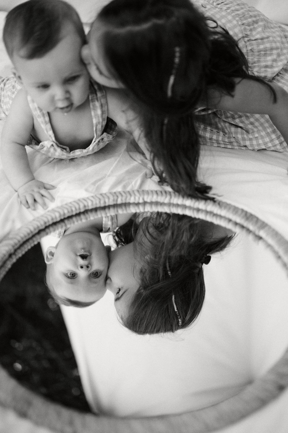 Black and white photo of siblings with baby and girl reflected in round mirror.