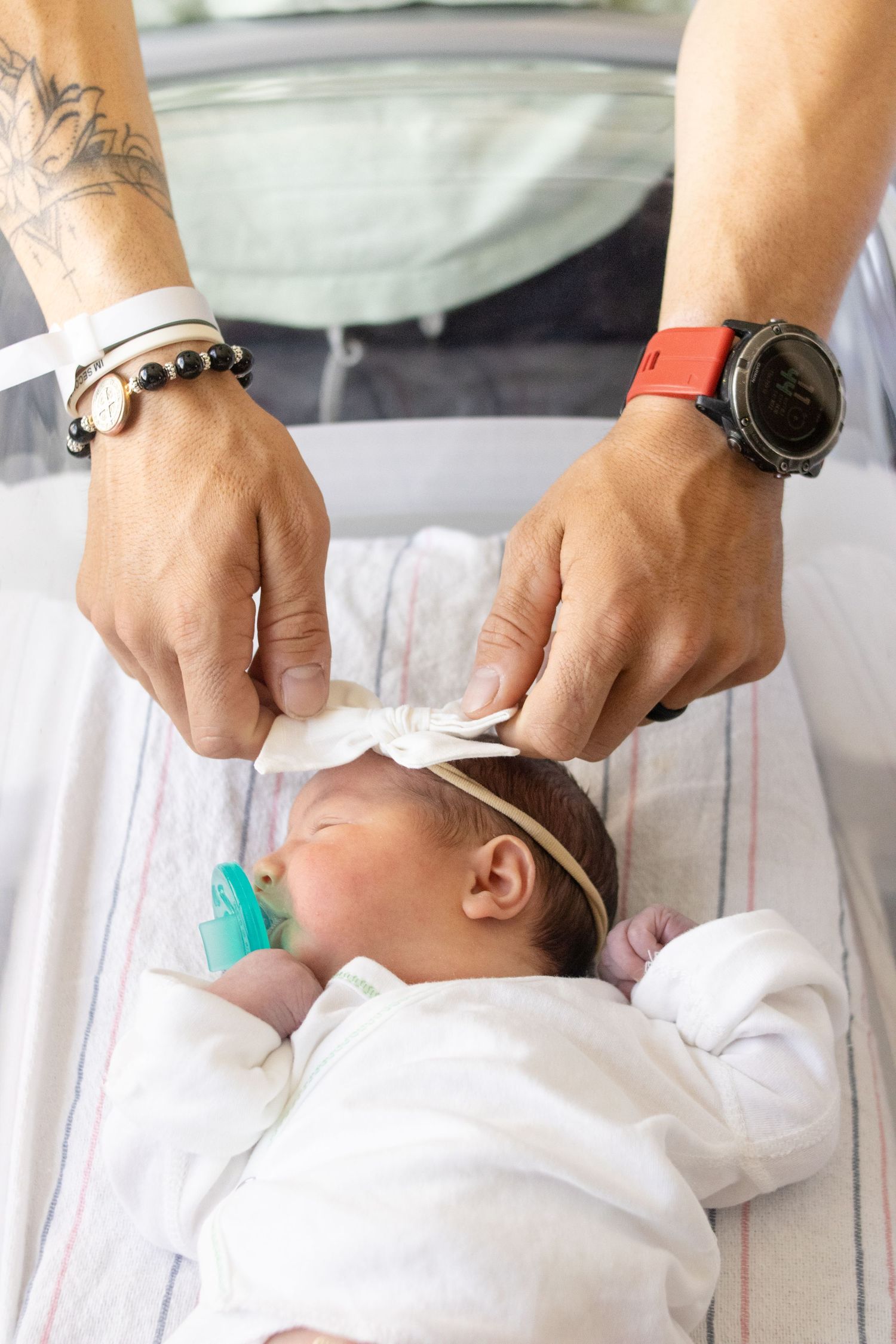 Dad fixing newborn baby girl bow while laying in hospital bassinet