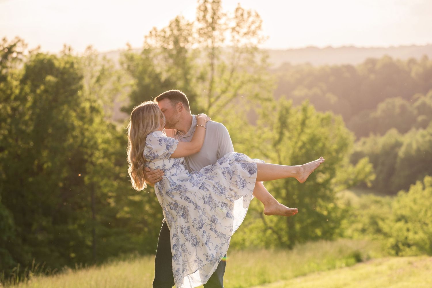 Silhouettes of couple embracing in sunset light with vintage airplane in grassy field.