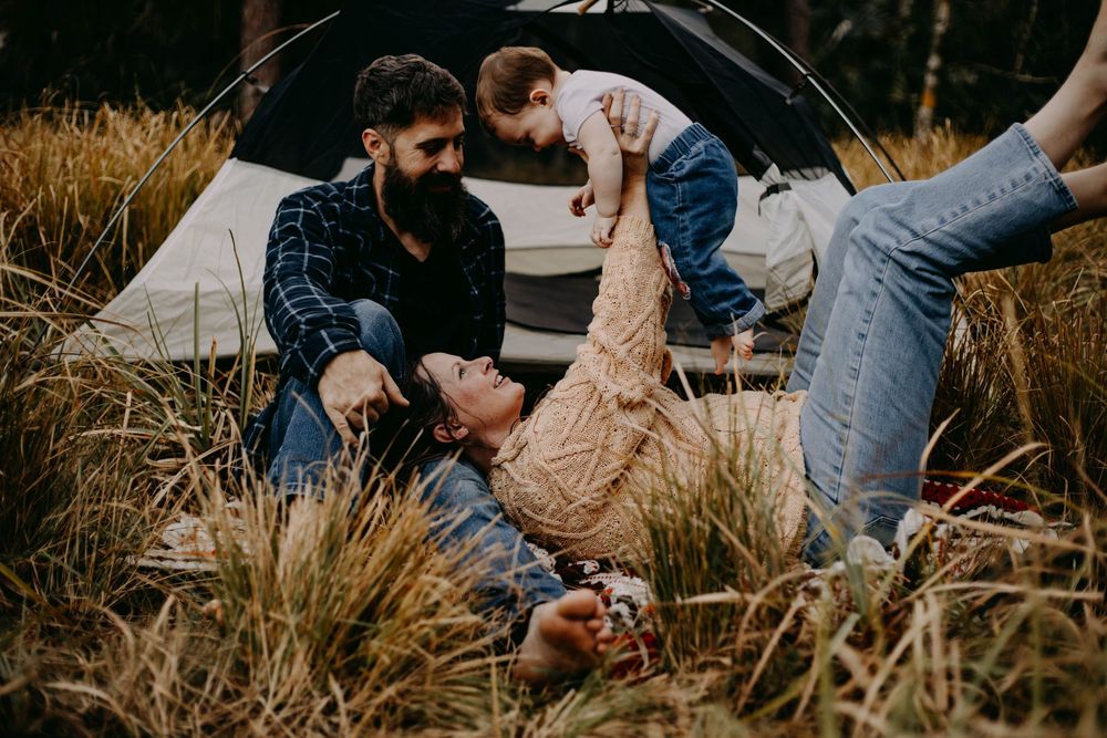 Couple relaxing together in tall grass near a car during golden hour.