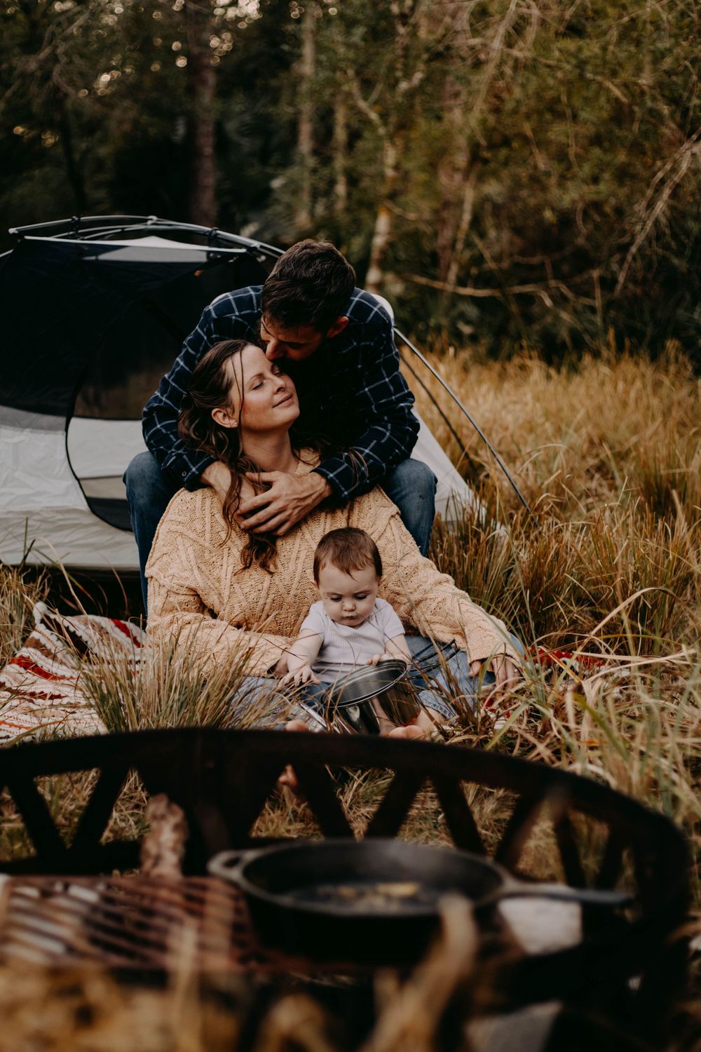 A tender family moment captured in warm autumn sunlight as they relax together outdoors on a blanket.