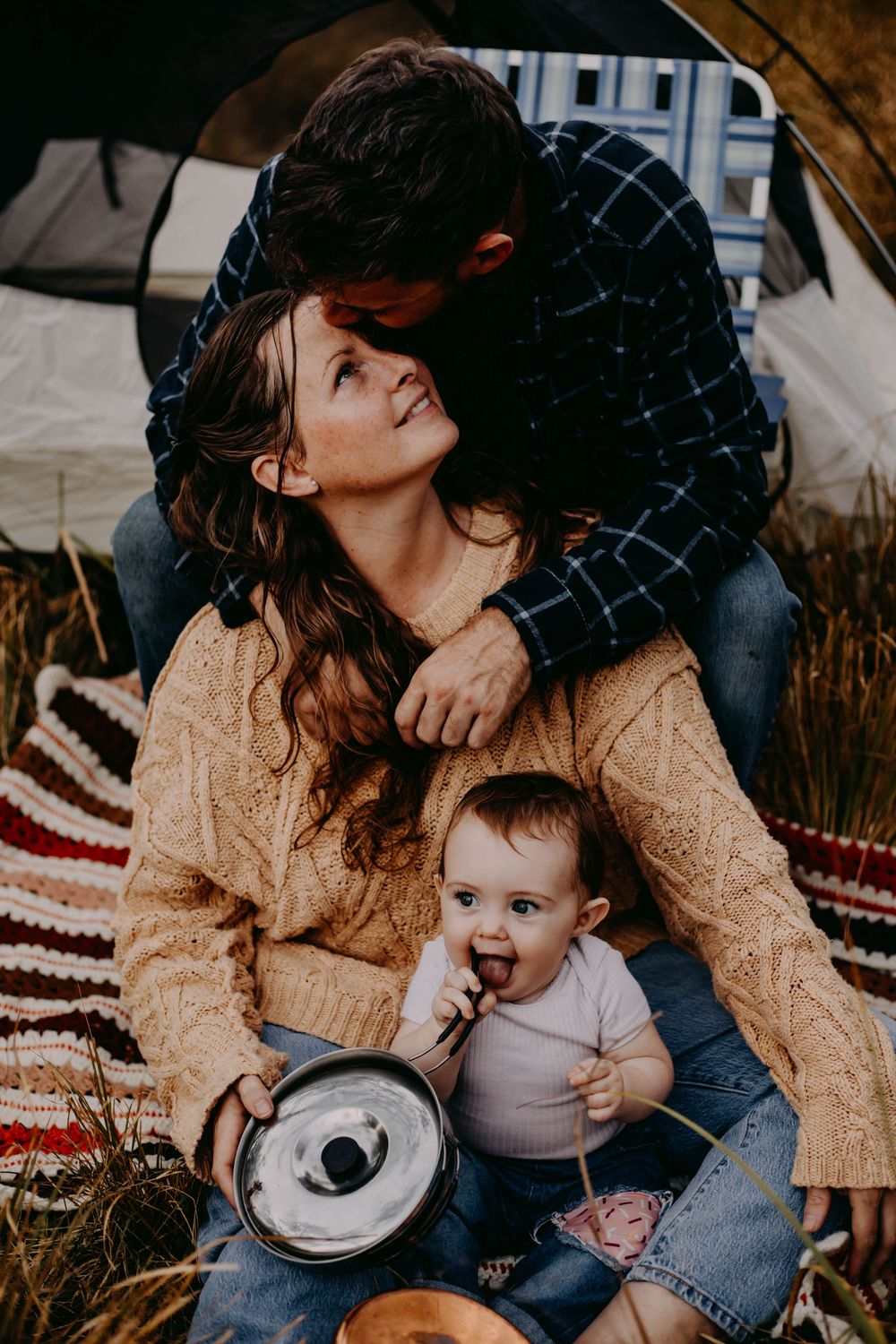Family sharing intimate moments on a blanket outdoors with a baby in casual attire.