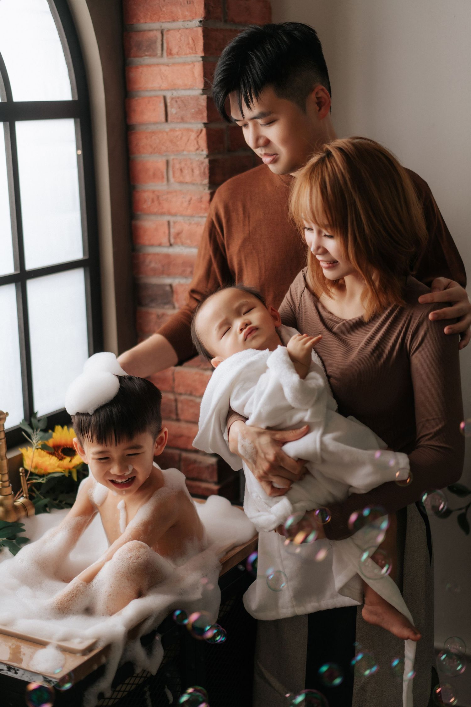 Family members in white outfits share joyful moments together against a brick wall background.