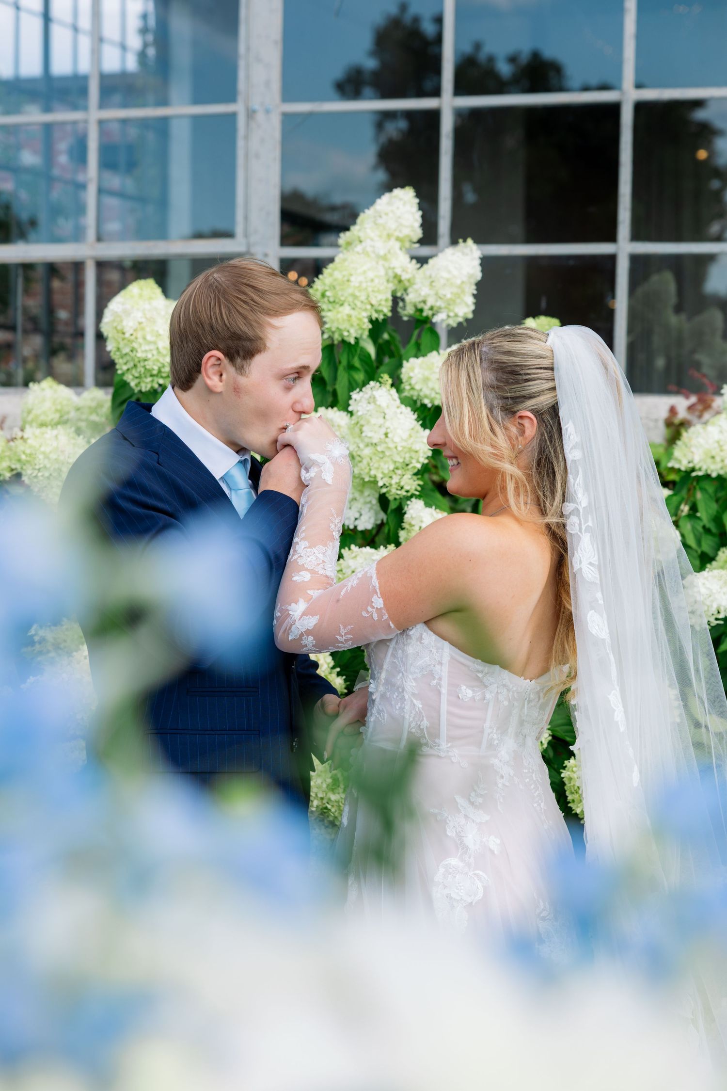 Wedding ceremony in a bright industrial venue with floor-to-ceiling windows and elegant floral arrangements.