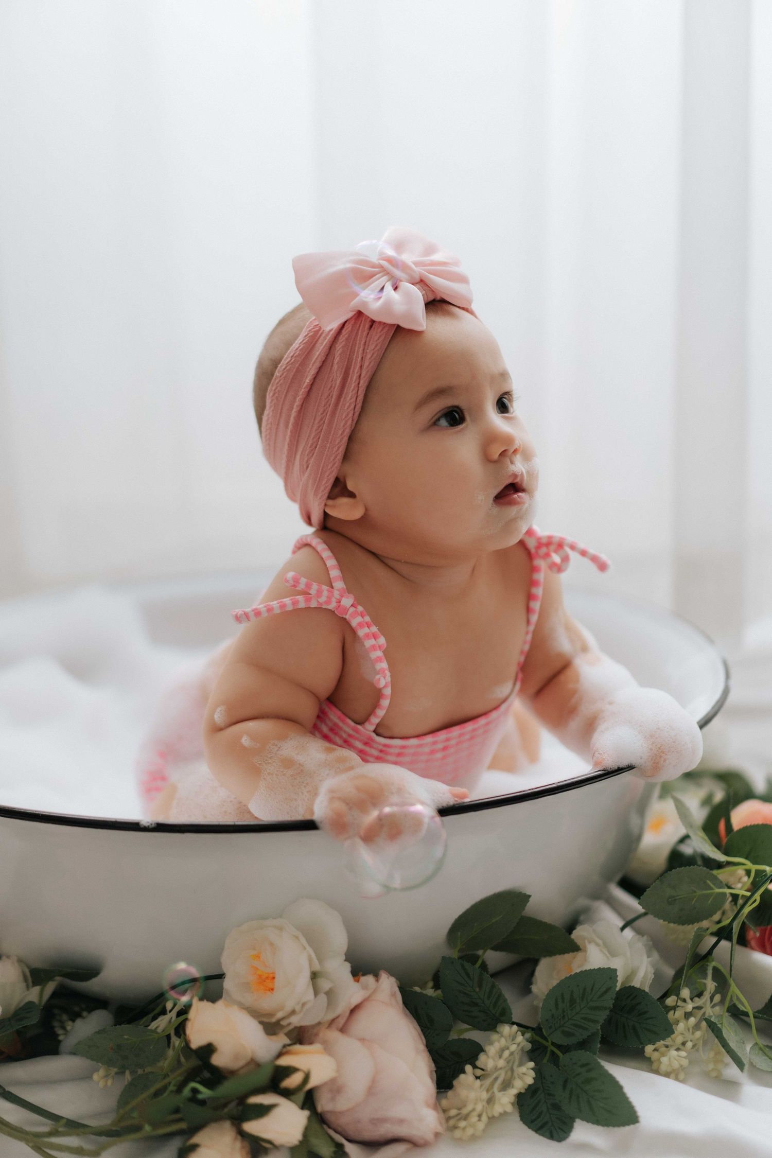 Baby sits on wooden floor surrounded by teal and white balloons during first birthday photoshoot.