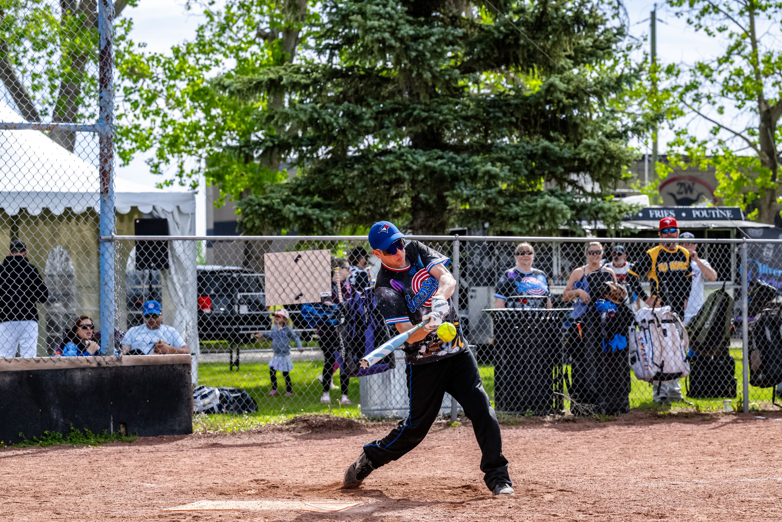 Baseball players in action during a game on a dirt field with spectators watching from behind the fence.
