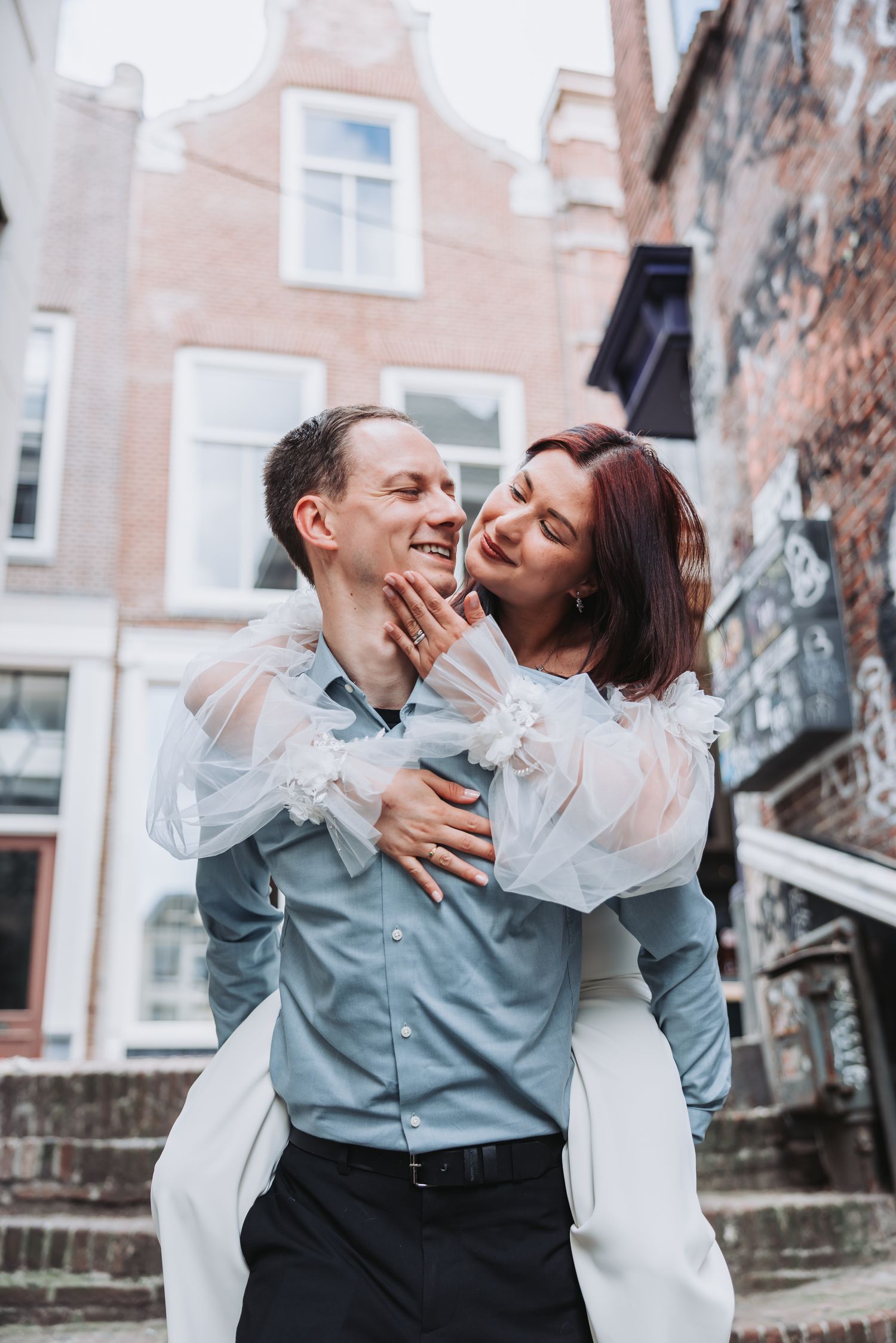 A romantic couple embraces on stone steps in front of historic buildings, sharing a tender moment