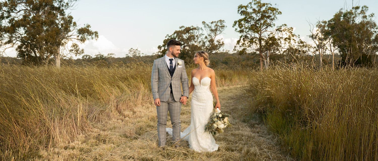 Bride and groom hold hands walking through golden grass fields during their outdoor wedding photoshoot.