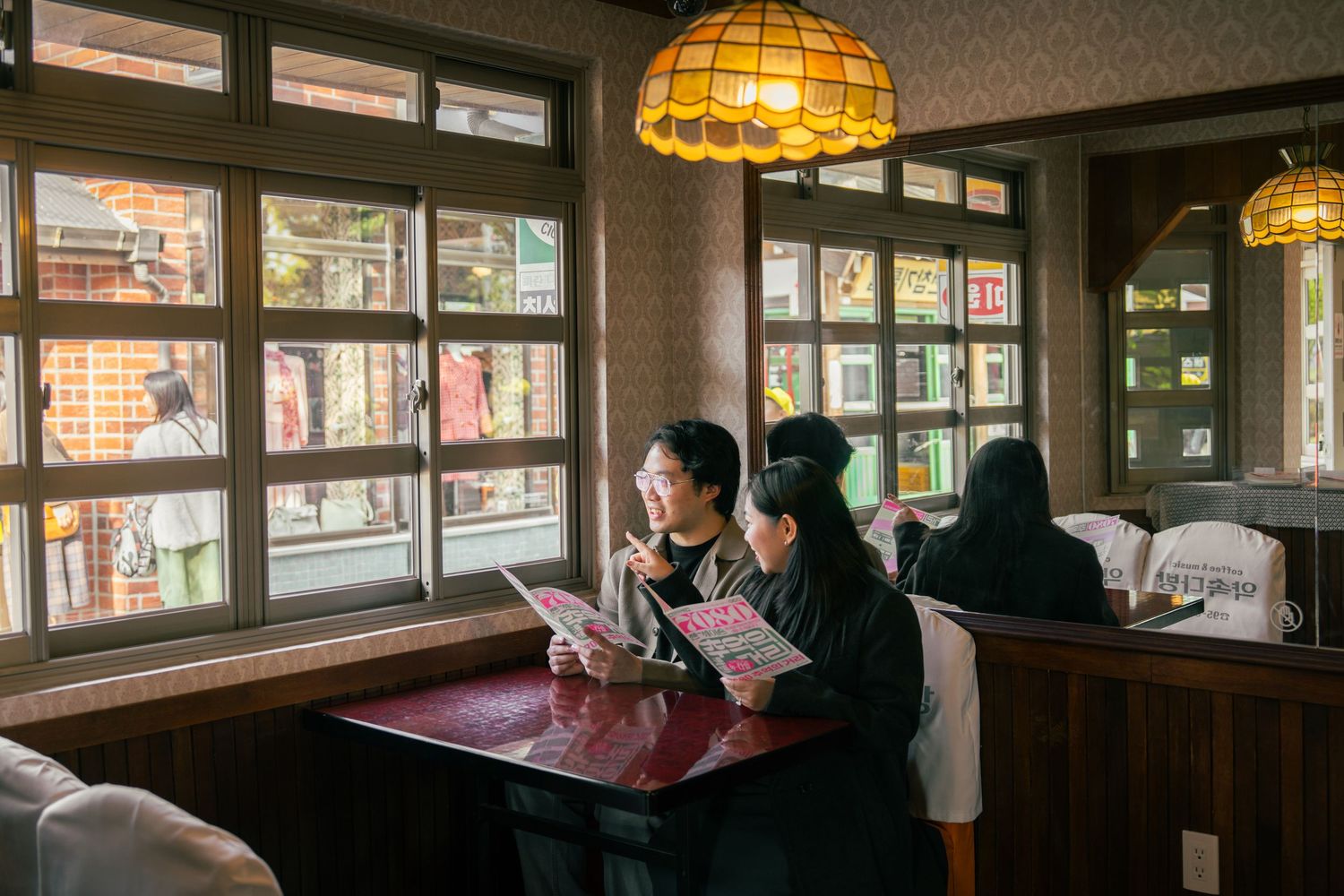 People sit at tables inside a cozy bar or restaurant with warm amber lighting from vintage pendant lamps overhead.
