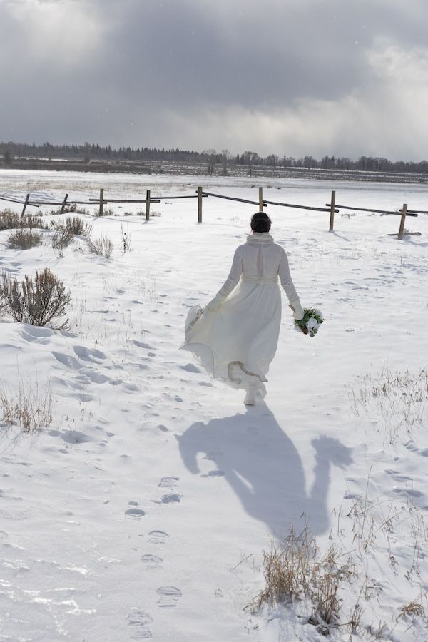 A series of white ghost-like sheets on poles create an eerie winter scene across a snowy field on a cloudy day.