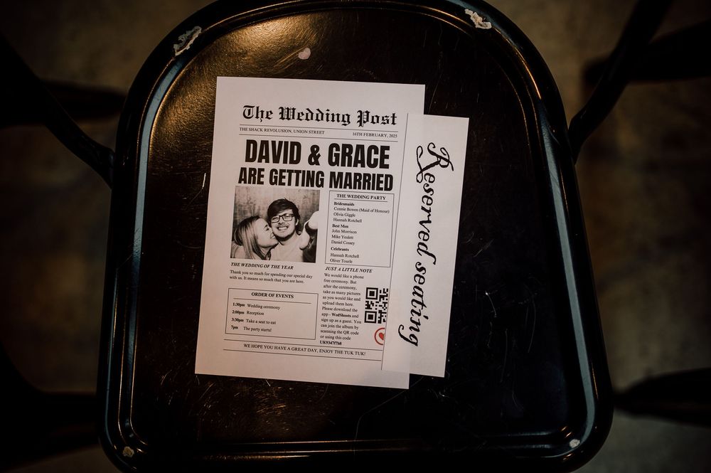 A black leather briefcase sits open with a wedding invitation and newspaper announcement visible inside.