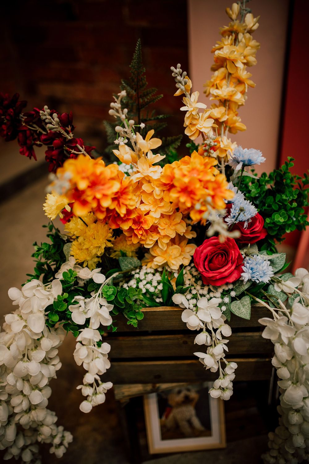 A decorative floral arrangement with cascading white orchids and vibrant yellow and orange blooms against a dark background.