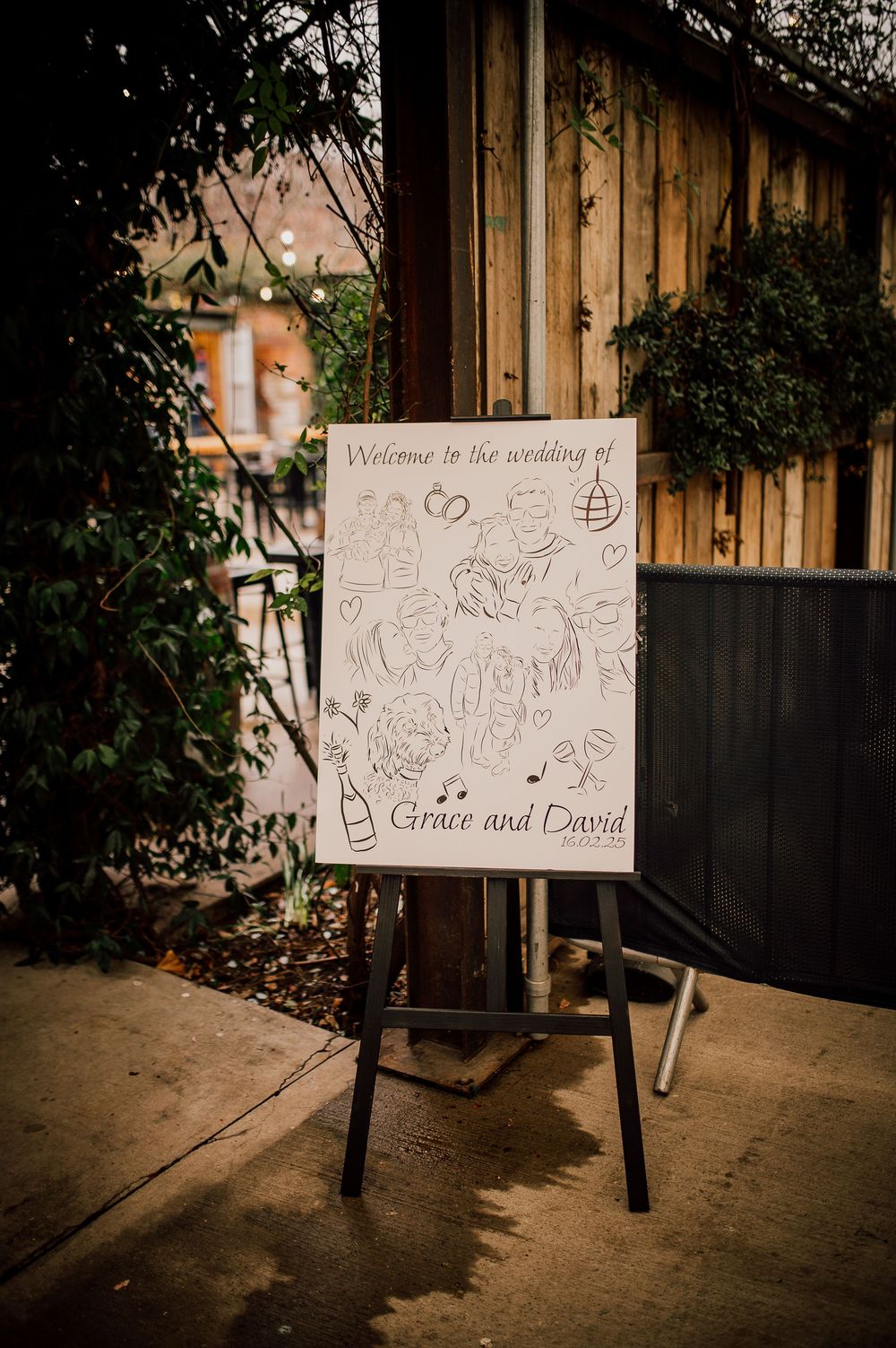 Hand-drawn welcome sign on white board displayed against wooden fence backdrop.