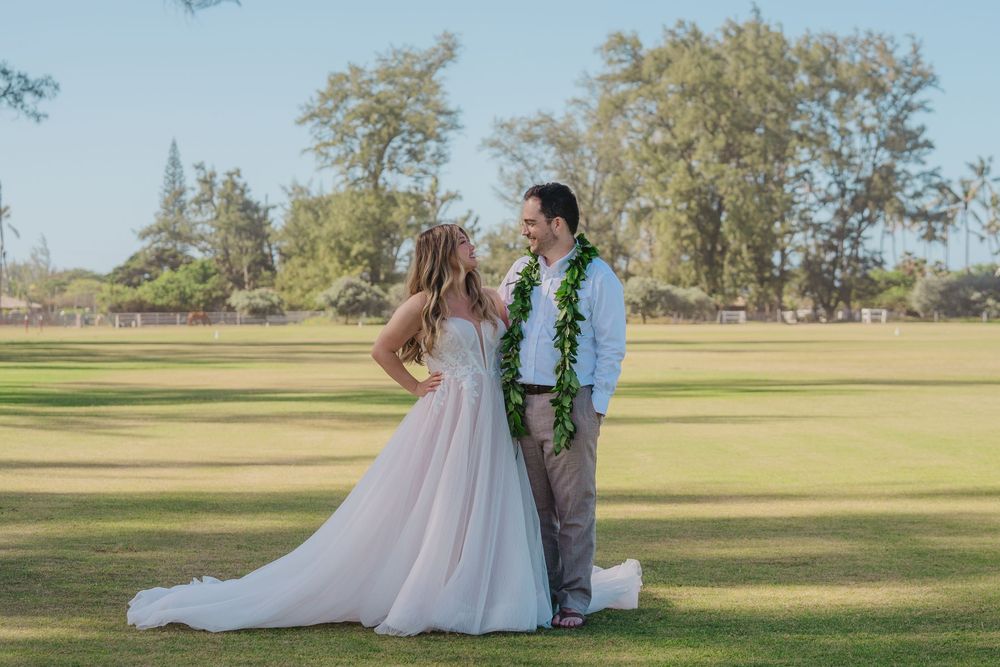 A romantic wedding couple poses in a scenic outdoor setting with golden sunlight and trees in the background.
