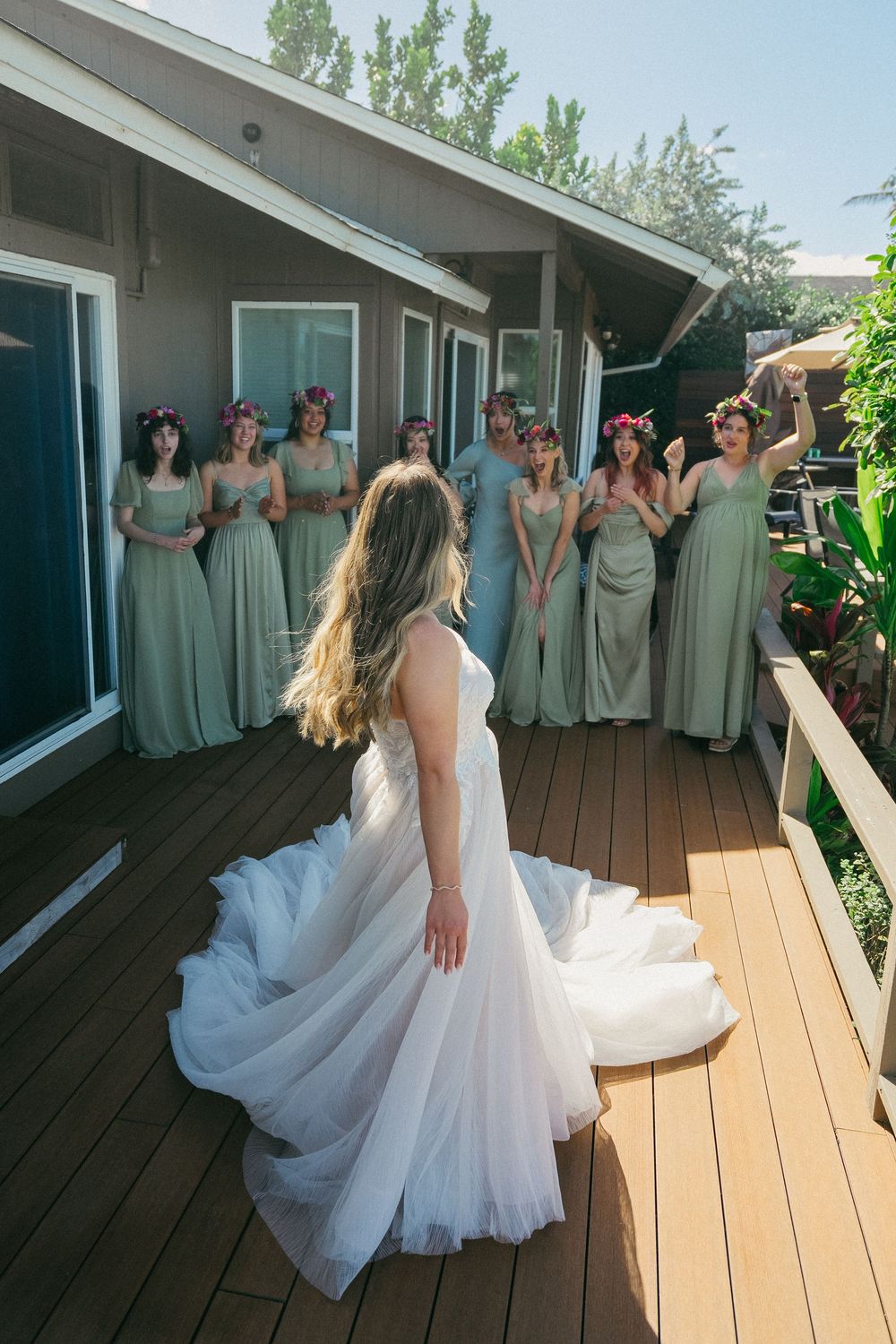 Wedding party in sage green bridesmaid dresses posing on a wooden deck.